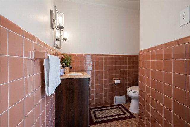 half bath with vanity, a wainscoted wall, tile walls, toilet, and tile patterned floors