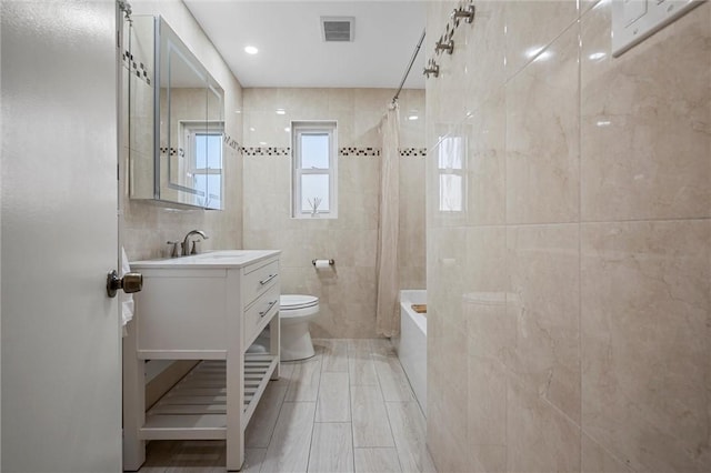 bathroom featuring vanity, visible vents, tile walls, toilet, and shower / tub combo with curtain