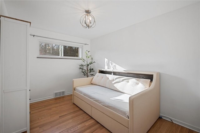 bedroom with a notable chandelier, wood finished floors, visible vents, and baseboards