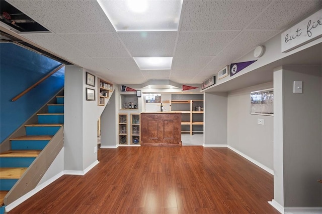 finished basement with a drop ceiling, baseboards, wood finished floors, and stairs