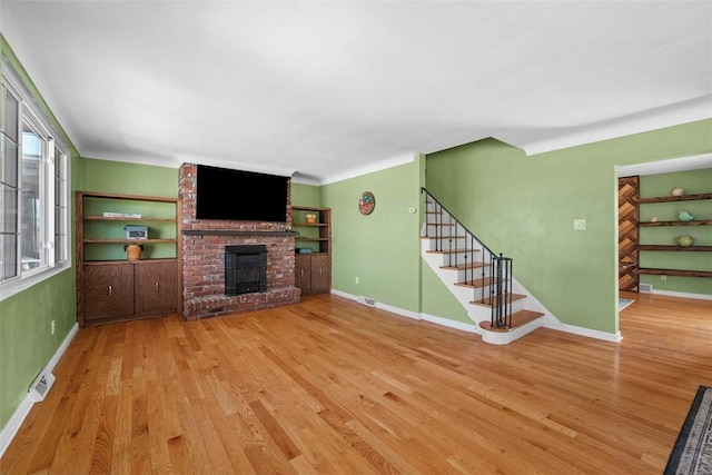 unfurnished living room featuring wood finished floors, stairway, a fireplace, and baseboards