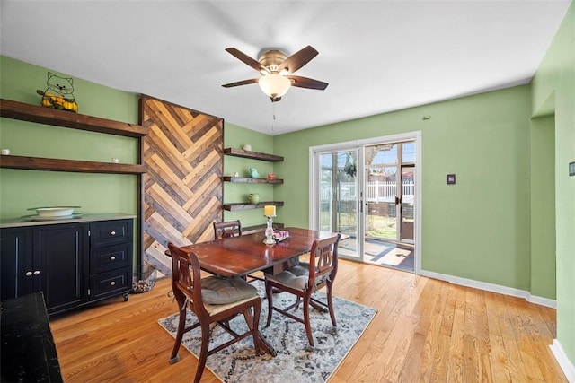 dining room with an accent wall, a ceiling fan, baseboards, and light wood finished floors