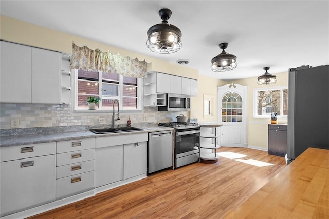 kitchen with light wood finished floors, backsplash, open shelves, appliances with stainless steel finishes, and a sink