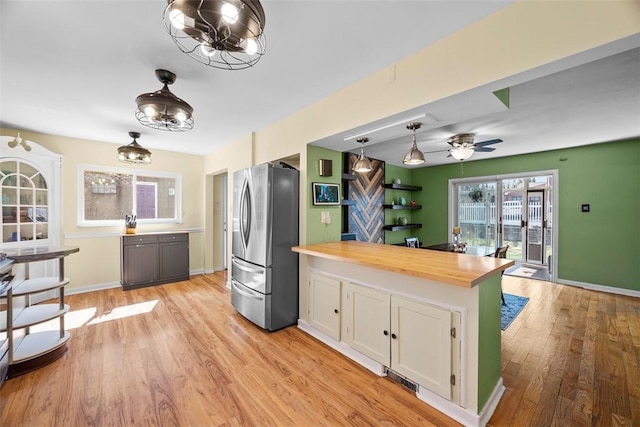 kitchen with baseboards, butcher block counters, light wood-style flooring, freestanding refrigerator, and white cabinets