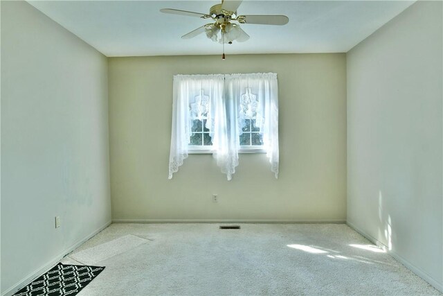 carpeted spare room with visible vents, baseboards, and ceiling fan