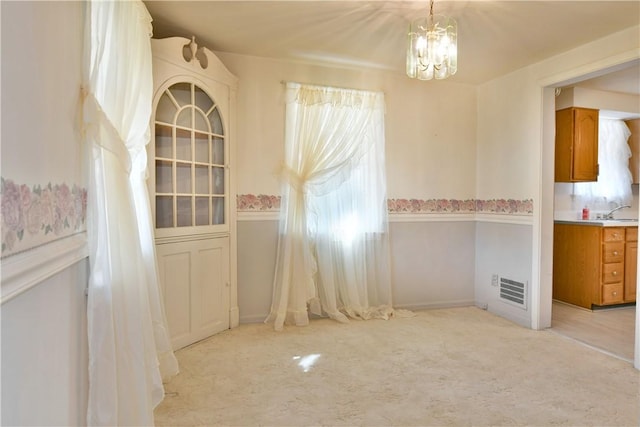 unfurnished dining area featuring visible vents, light colored carpet, an inviting chandelier, and a sink