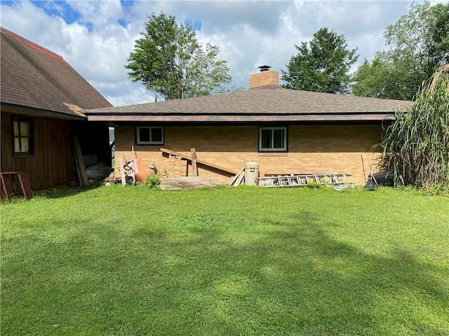 back of property with brick siding, a shingled roof, a chimney, and a lawn