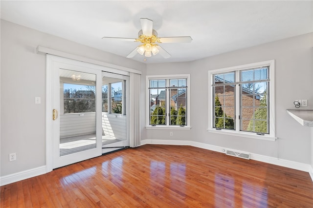 empty room with visible vents, ceiling fan with notable chandelier, baseboards, and hardwood / wood-style flooring