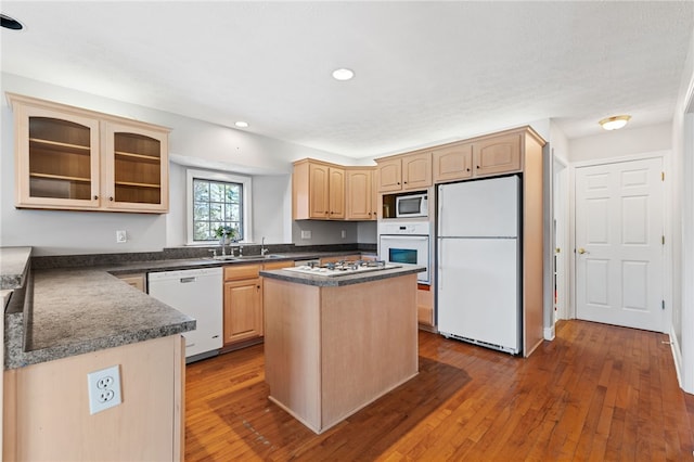 kitchen with white appliances, light brown cabinets, wood-type flooring, and a sink