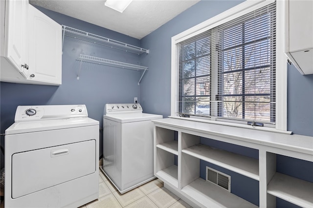 washroom featuring washing machine and dryer, cabinet space, a textured ceiling, and visible vents