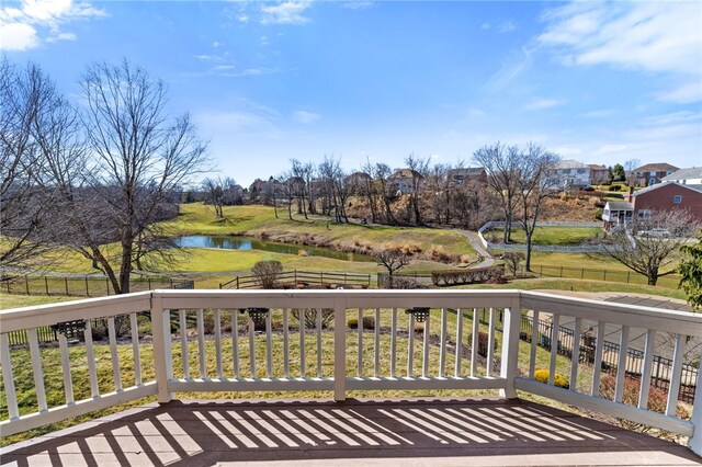 wooden terrace with a water view, a lawn, and fence