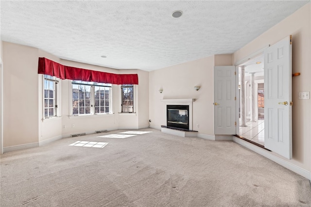 unfurnished living room with visible vents, baseboards, a glass covered fireplace, and carpet floors