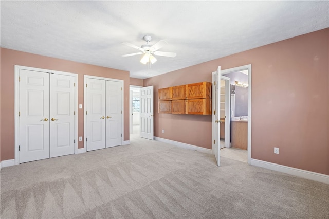 unfurnished bedroom with light carpet, two closets, and baseboards