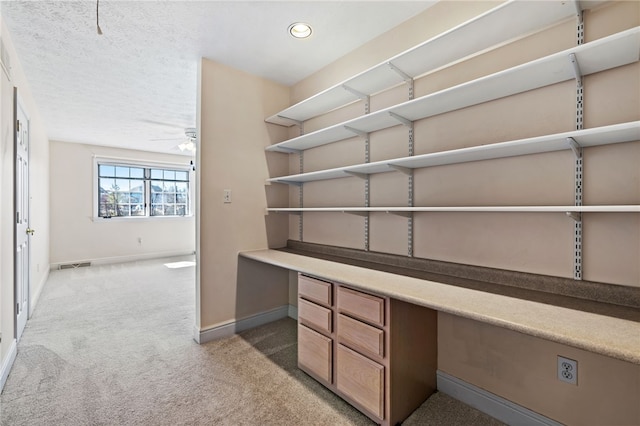 unfurnished office with a ceiling fan, visible vents, baseboards, built in desk, and light carpet