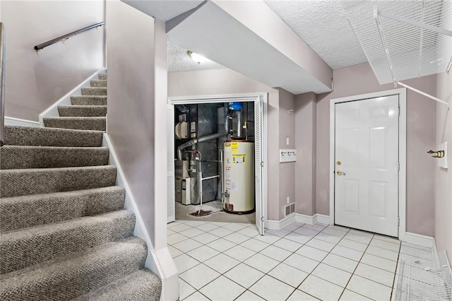 foyer entrance with visible vents, a textured ceiling, gas water heater, stairway, and light tile patterned flooring