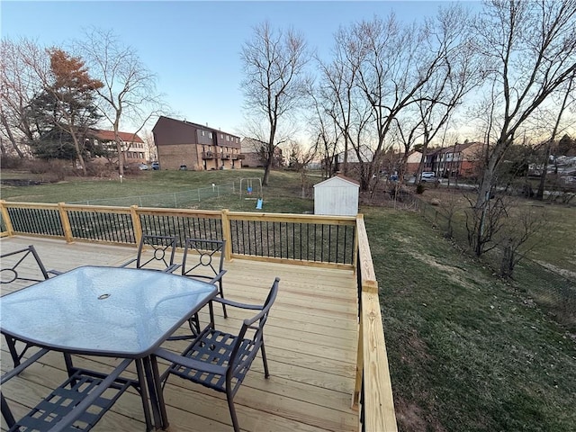 wooden deck with an outbuilding, a lawn, outdoor dining space, and a shed