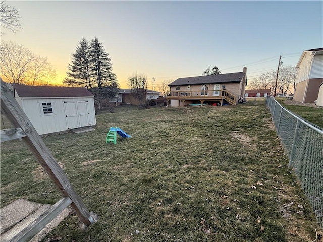 yard at dusk featuring a storage shed, an outbuilding, a fenced backyard, and a wooden deck