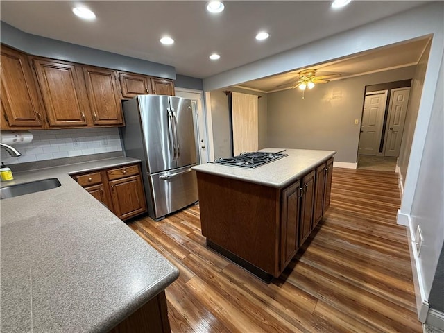 kitchen with wood finished floors, a kitchen island, a sink, stainless steel appliances, and tasteful backsplash