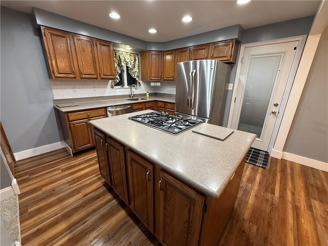 kitchen with brown cabinetry, dark wood-style flooring, a sink, appliances with stainless steel finishes, and backsplash