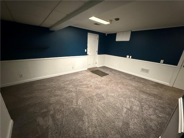 empty room with a wainscoted wall, dark carpet, visible vents, and a drop ceiling