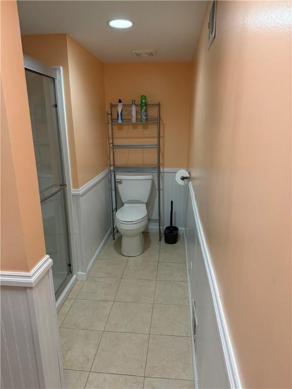 bathroom featuring tile patterned flooring, visible vents, a wainscoted wall, toilet, and a stall shower