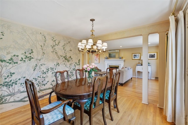 dining space with wallpapered walls, a fireplace, light wood-style floors, crown molding, and a chandelier