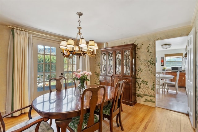 dining space featuring wallpapered walls, ornamental molding, light wood finished floors, and a chandelier