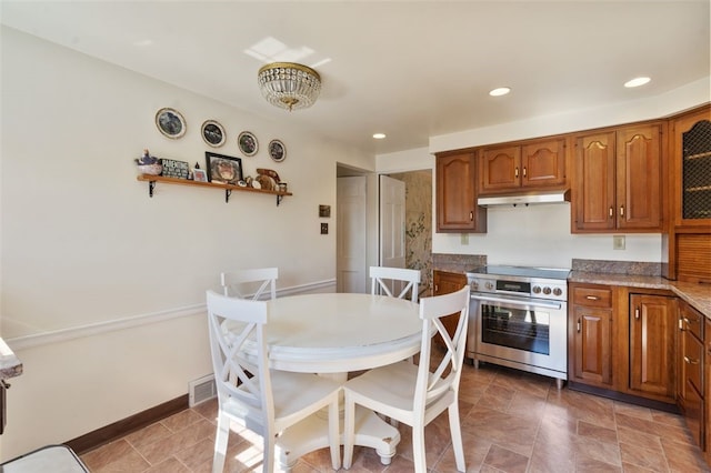 kitchen featuring baseboards, visible vents, high end stove, under cabinet range hood, and brown cabinets