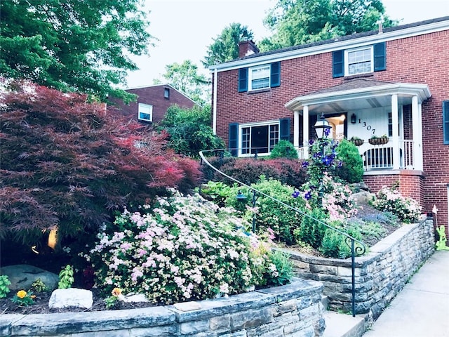 colonial house featuring brick siding, covered porch, and a chimney