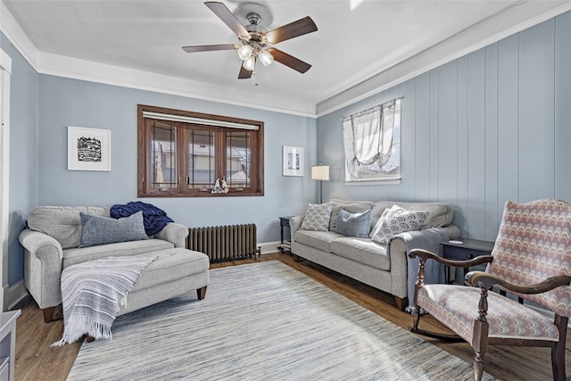 living area featuring radiator, a ceiling fan, wood finished floors, baseboards, and crown molding