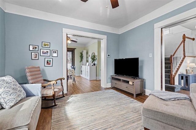 living room with stairway, crown molding, a ceiling fan, and wood finished floors