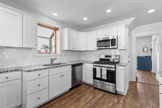 kitchen with a sink, dark wood finished floors, appliances with stainless steel finishes, white cabinets, and light stone countertops