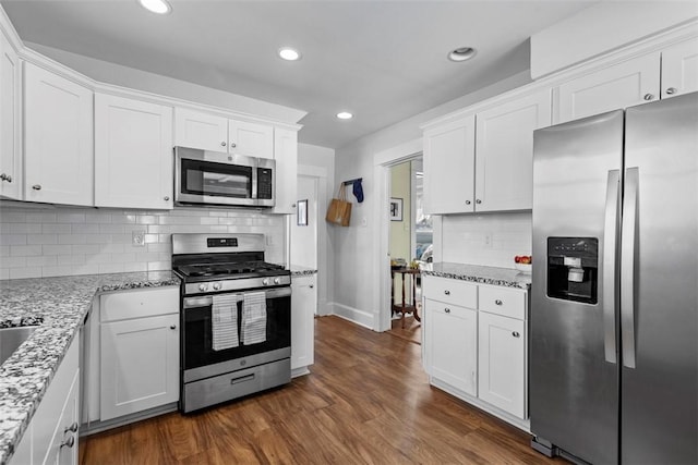 kitchen with backsplash, dark wood finished floors, stainless steel appliances, white cabinets, and light stone countertops