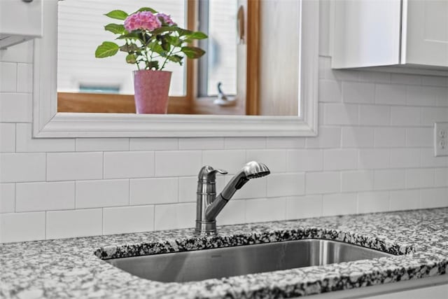 room details featuring tasteful backsplash, white cabinetry, light stone counters, and a sink