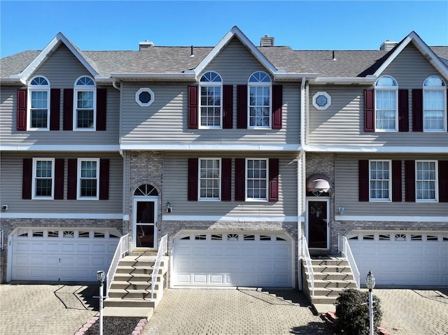 view of front facade with brick siding, driveway, an attached garage, and roof with shingles