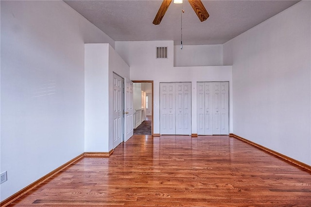 unfurnished bedroom with wood finished floors, visible vents, baseboards, ceiling fan, and two closets