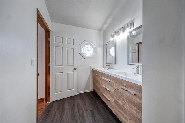 bathroom with double vanity, wood finished floors, lofted ceiling, and a sink