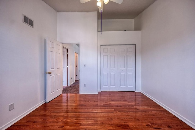 unfurnished bedroom with wood finished floors, visible vents, a towering ceiling, and baseboards