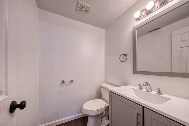 bathroom with visible vents, toilet, a textured ceiling, wood finished floors, and vanity