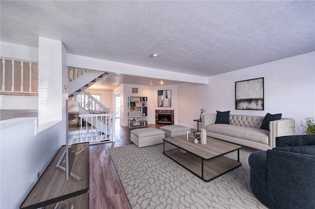 living area with a fireplace, a textured ceiling, stairs, and wood finished floors