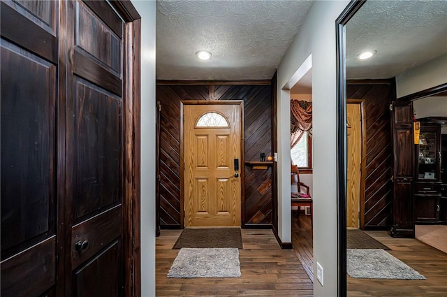 foyer entrance with wood walls, a textured ceiling, and wood finished floors