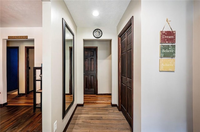 corridor featuring a textured ceiling, baseboards, and dark wood-style flooring