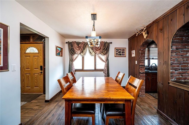 dining room featuring dark wood-style floors, wooden walls, a textured ceiling, and baseboards