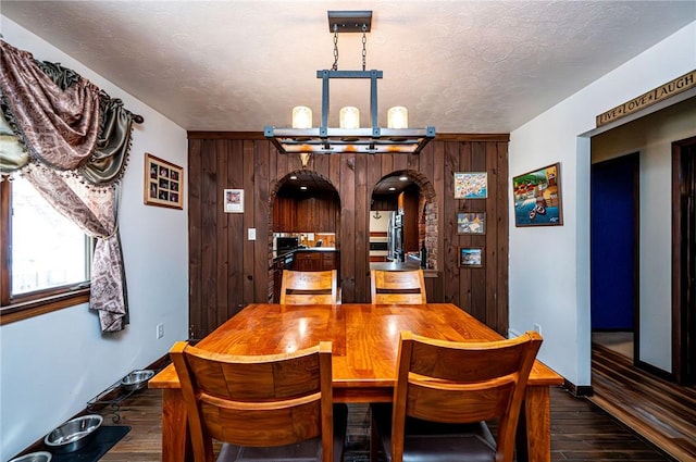 dining room featuring baseboards, wood walls, arched walkways, dark wood-style floors, and a textured ceiling