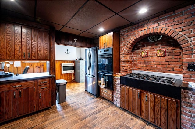 kitchen featuring brick wall, light wood-style flooring, heating unit, black appliances, and a paneled ceiling