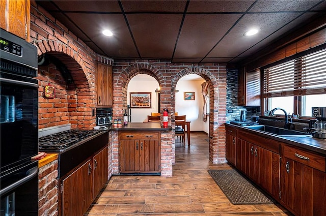 kitchen featuring light wood-type flooring, black appliances, a sink, dark countertops, and a peninsula