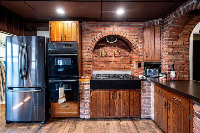 kitchen featuring cooktop, freestanding refrigerator, wood finished floors, brown cabinetry, and dobule oven black