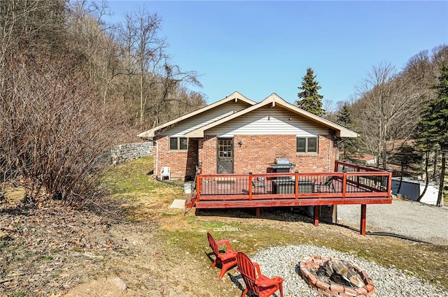 back of property featuring brick siding, an outdoor fire pit, and a deck