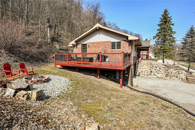 back of property featuring brick siding, a wooden deck, and an outdoor fire pit