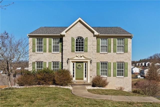 colonial house with a front lawn, brick siding, and a shingled roof